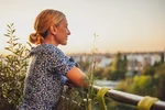 Eine Frau steht auf einem Balkon und genießt den schönen Ausblick im Abendlicht. 