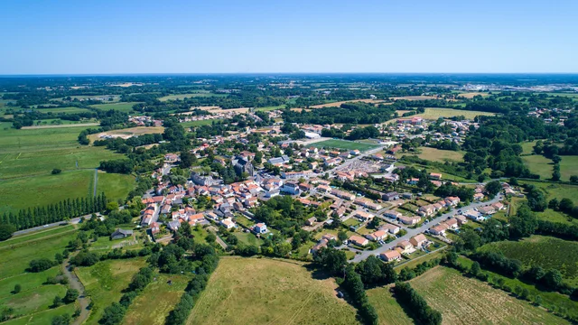 Luftaufnahme eines kleinen Dorfes, das in mitten grüner Felder liegt.