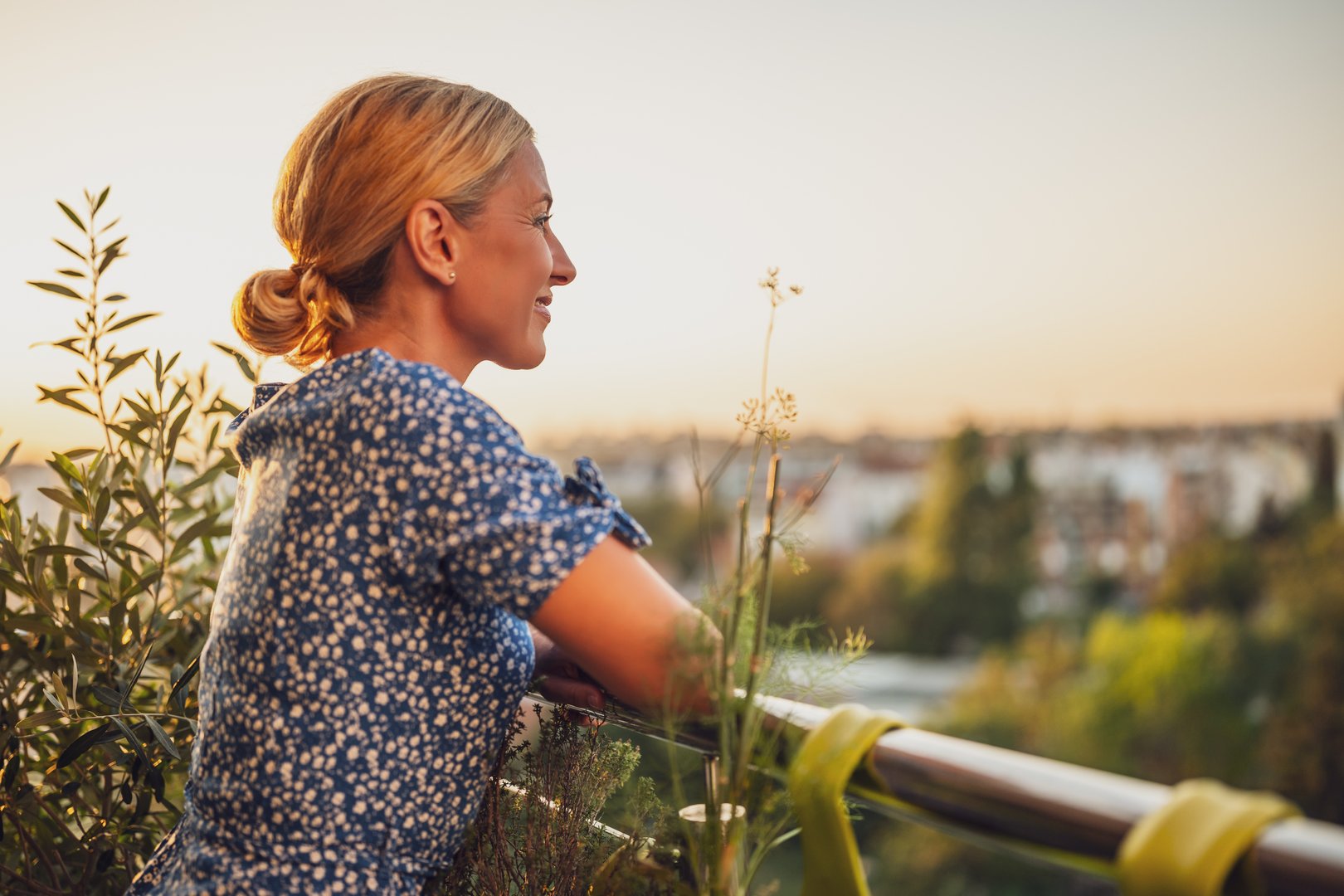 Eine Frau steht auf einem Balkon und genießt den schönen Ausblick im Abendlicht. 